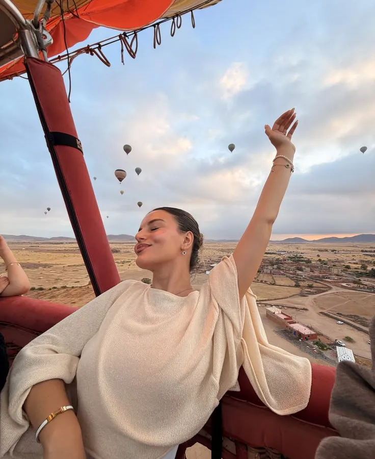 Voyageuse bras levés dans la nacelle, montgolfières et Atlas au lever du soleil